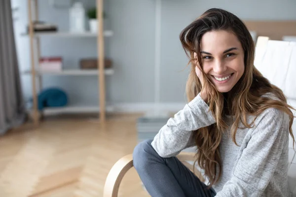 Närbild porträtt av vackra lycklig kvinna tittar på kameran och ler medan du sitter i en mysig stol. — Stockfoto