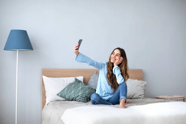 Hermosa mujer feliz en casa en el sofá hacer selfie en el teléfono celular . —  Fotos de Stock