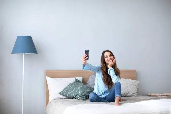 Hermosa mujer feliz en casa en el sofá hacer selfie en el teléfono celular . —  Fotos de Stock