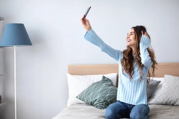 Prise de vue d'une jeune femme heureuse prenant selfie avec son téléphone portable tout en étant assis au salon . — Photo