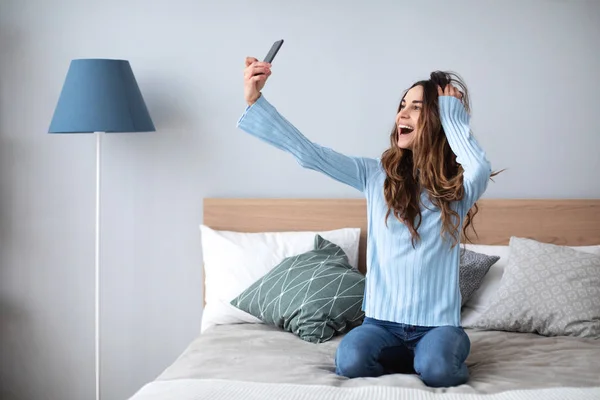 Tiro de uma jovem feliz tomando selfie com seu celular enquanto sentado na sala de estar . — Fotografia de Stock