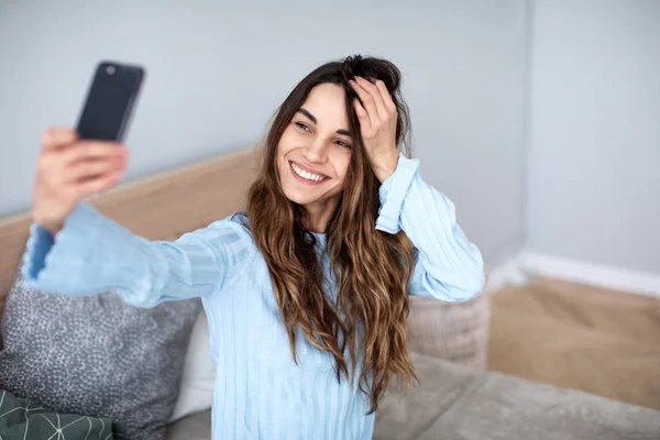 Hermosa joven sonriente mujer con un teléfono en sus manos toma una selfie . —  Fotos de Stock