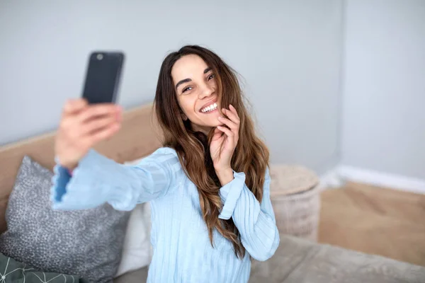 Hermosa mujer sonriente con un teléfono toma una selfie en casa . —  Fotos de Stock