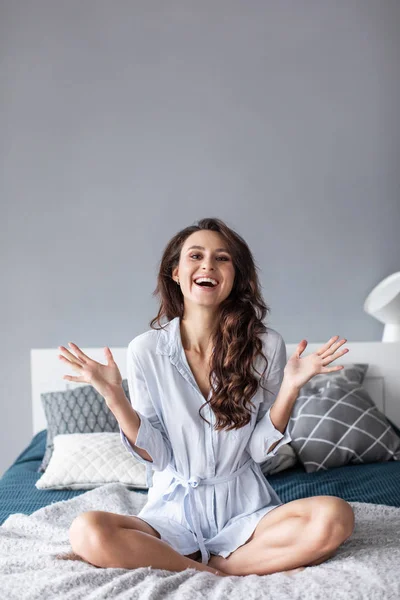 Aantrekkelijke jonge vrouw die lacht op het bed thuis. — Stockfoto