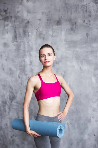 Portrait of cheerful woman holding exercise mat indoors. — Stock Photo, Image