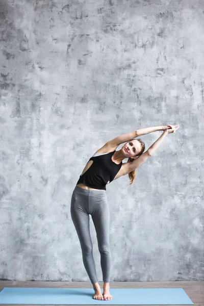 Chica haciendo ejercicios de yoga en una esterilla de yoga azul de cuerpo entero en el estudio . —  Fotos de Stock