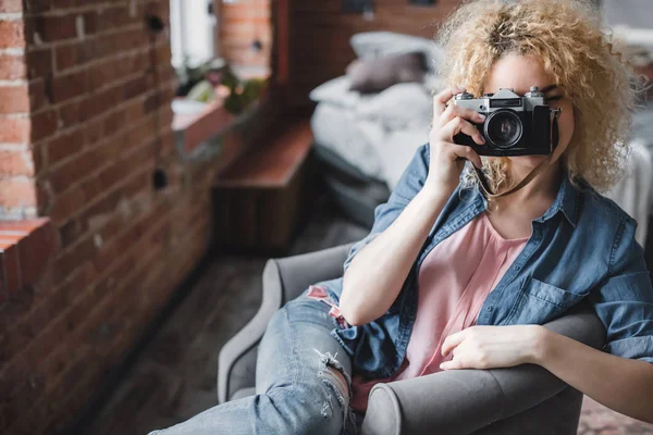 Curly blonde woman with a retro photo camera at home. — Stock Photo, Image