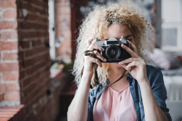 Curly blonde woman holding her retro photo camera at home. — Stock Photo, Image