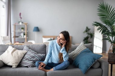 Gülümseyen kadın kanepede evde telefonda konuşurken. 