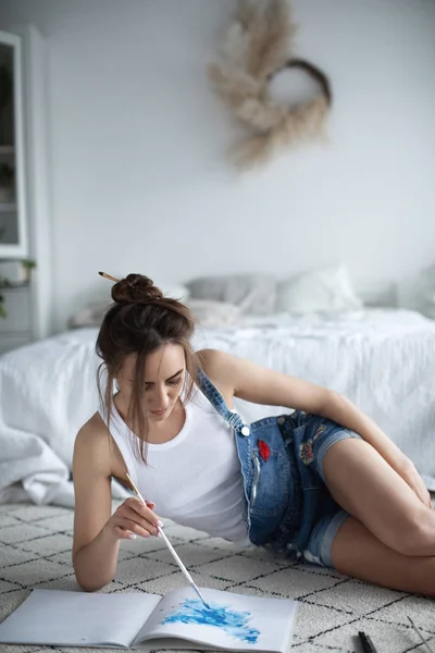 Junge schöne Künstlerin. einen Himmel in das Album malen, der zu Hause auf dem Boden sitzt. — Stockfoto