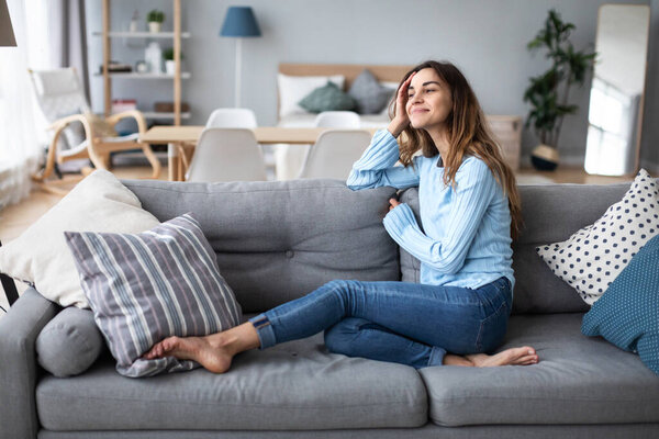 Tranquil smiling millennial woman leaning on sofa. Domestic life.