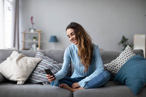 Улыбающаяся молодая женщина дома с помощью современного смартфона. Онлайн чат
.
