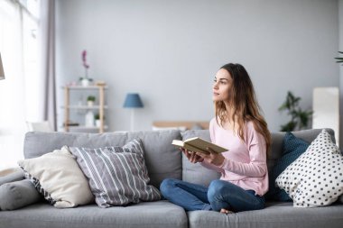 Evdeki kadın kanepede oturup kitap okuyor. Evde eğitim.