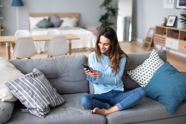 Улыбающаяся молодая женщина дома с помощью современного смартфона. Онлайн чат. Домашняя жизнь
.
