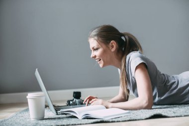 Dizüstü bilgisayar kullanan genç bir kadın, müşteriyle internet üzerinden iletişim kuruyor. Evdeki rahat ofis işyeri.