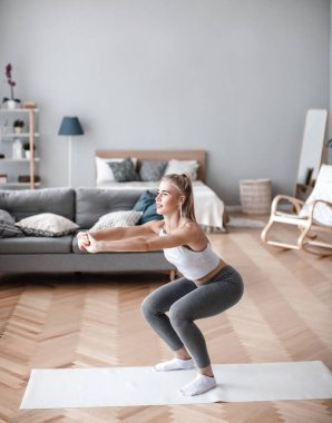 Spor giyimli formalı kadın evde çömelme egzersizleri yapıyor. İçerde fiziksel egzersiz..