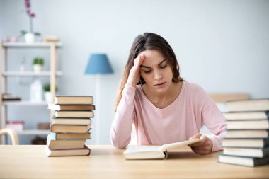Sınav için kitap okuyan ya da ödev yapan üzgün kız öğrenci. Ev eğitimini kabul et.