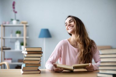 Evde kitaplarla dolu bir masada oturan mutlu genç bir kadın. Konsept öğrenimi.