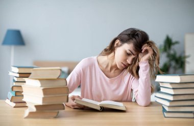 Kitapları olan üzgün genç bir kadın çalışma masasında oturuyor. Ev eğitimi kavramı.