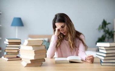 Kitapları olan üzgün genç bir kadın çalışma masasında oturuyor. Ev eğitimi kavramı.