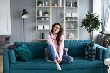 Oturma odasındaki kanepede gülümseyen güzel bir kadın. Evde kalan bir kızın portresi..