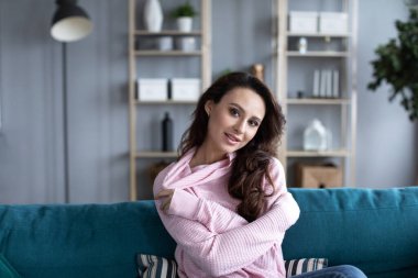 Oturma odasındaki kanepede gülümseyen güzel bir kadın. Evde kalan bir kızın portresi..