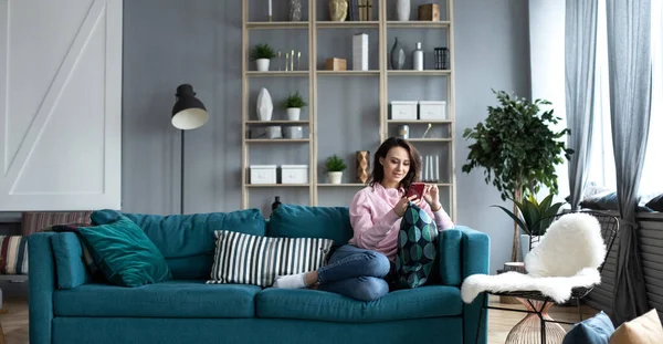 Evde akıllı telefonu olan güzel, gülümseyen bir kadın. Cep telefonu kullan.