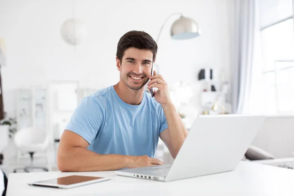 Jovem Alegre Roupas Casuais Sentado Mesa Com Laptop Falando Smartphone — Fotografia de Stock