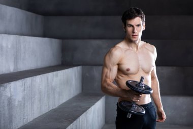 Spor salonunda dambılla egzersiz yapan kararlı, genç ve çekici bir adam..