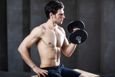 Spor salonunda dambılla egzersiz yapan kararlı, genç ve çekici bir adam..