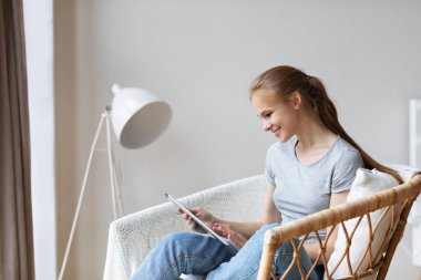 Genç bir kadın rahat koltuğunda dijital tablet kullanıyor. Görüntülü sohbet izle.