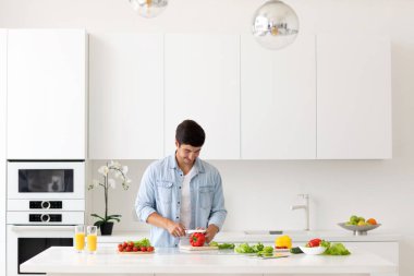 Modern ışık mutfağında salata için sebze doğrayan genç bir adam. Vejetaryen konsepti.
