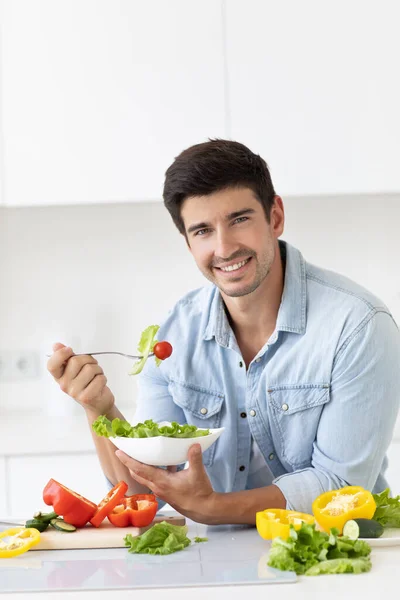 カメラを見ているサラダ新鮮な野菜のプレートとハンサムな笑顔の若い男 キッチンで幸せなカジュアル男の肖像画 — ストック写真
