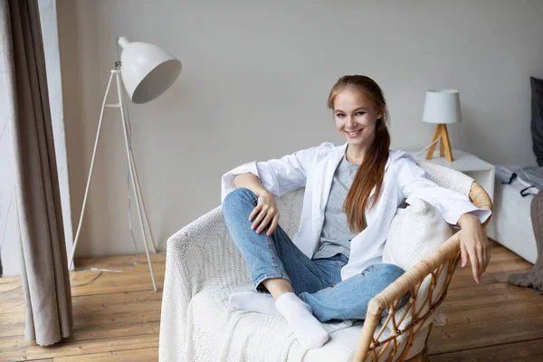 Gülümseyen bin yıllık kızıl saçlı kız evdeki koltukta dinleniyor. Stressiz hissediyor. Evde keyifli bir hafta sonu..