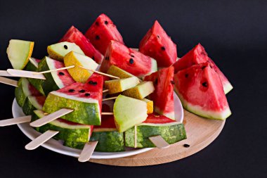 Taze, olgun karpuz ve kavun dilimlenmiş ahşap tabakta karpuz çekirdekleri, siyah arka planda tahta çubuklar, kapat
