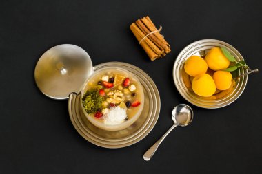 Traditional Turkish Dessert,Asure or Noah's Ark Pudding on black surface with fresh apricot fruit,cinnamon sticks and spoon.Ashure Day Concept.