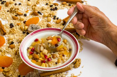 Eski bir el, Ashure Dish 'in malzemeleri üzerine beyaz kaseden ashura tatlısı yer.