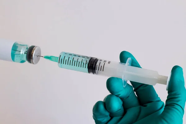 Gloved hand holding syringe,push needle into drug glass bottle on white.Conceptual image of medical sector.