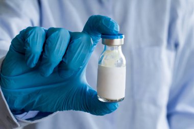 Mavi eldivenli doktor elinde küçük bir ilaç şişesi var ve etiketi boş. Tıbbi konsept.