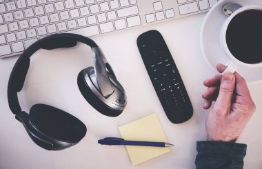 Yukarıdan bir resepsiyon, kulaklık, klavye, Not defteri ile çalışma alanı ve bir el bir fincan kahve almaya mans. İşten kır. Uygulanan tahıl etkiler ile stilize görüntü