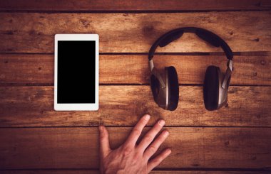 Birtakım kablosuz kulaklık ve boş tablet şablon bir rustik ahşap masanın üzerinde yatan bir üstten görünüm resepsiyon. Görüntüye eklenen stil ve tahıl etkisi.