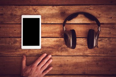 Birtakım kablosuz kulaklık ve boş tablet şablon bir rustik ahşap masanın üzerinde yatan bir üstten görünüm resepsiyon. Görüntüye eklenen stil ve tahıl etkisi.