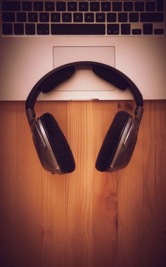 Birtakım kablosuz kulaklık ve dizüstü bir rustik ahşap masanın üzerinde yatan bir üstten görünüm resepsiyon. Görüntüye eklenen stil ve tahıl etkisi.