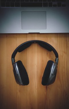 Birtakım kablosuz kulaklık ve dizüstü bir rustik ahşap masanın üzerinde yatan bir üstten görünüm resepsiyon. Görüntüye eklenen stil ve tahıl etkisi.