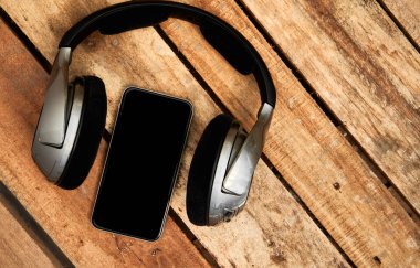 Üstten görünüm kablosuz kulaklık ve cep telefonu boş şablon bir rustik ahşap masanın üzerinde yatan bir dizi. Görüntüye eklenen stil ve tahıl etkisi.