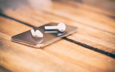 45 derece görüntü kablosuz earbud kulaklık ve cep telefonu bir rustik ahşap masanın üzerinde yatan bir dizi. Görüntüye eklenen stil ve tahıl etkisi.