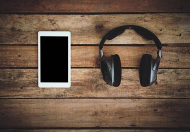 Birtakım kablosuz kulaklık ve boş tablet şablon bir rustik ahşap masanın üzerinde yatan bir üstten görünüm resepsiyon. Görüntüye eklenen stil ve tahıl etkisi.