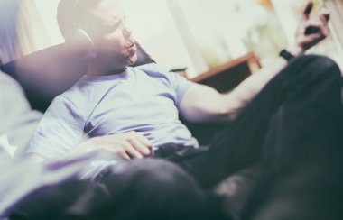 Zevk rahatlatıcı bir koltuk içinde kablosuz kulaklıklar müzik dinlemek ve hava gitar çalmak bir adam. Görüntüye eklenen stil ve tahıl etkisi.