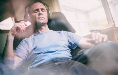 Rahatlatıcı bir koltuk kablosuz kulaklık müzik dinleme keyfi bir adam. Görüntüye eklenen stil ve tahıl etkisi.