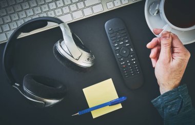 Yukarıdan bir resepsiyon, kulaklık, klavye, Not defteri ile çalışma alanı ve bir el bir fincan kahve almaya mans. İşten kır. Uygulanan tahıl etkiler ile stilize görüntü